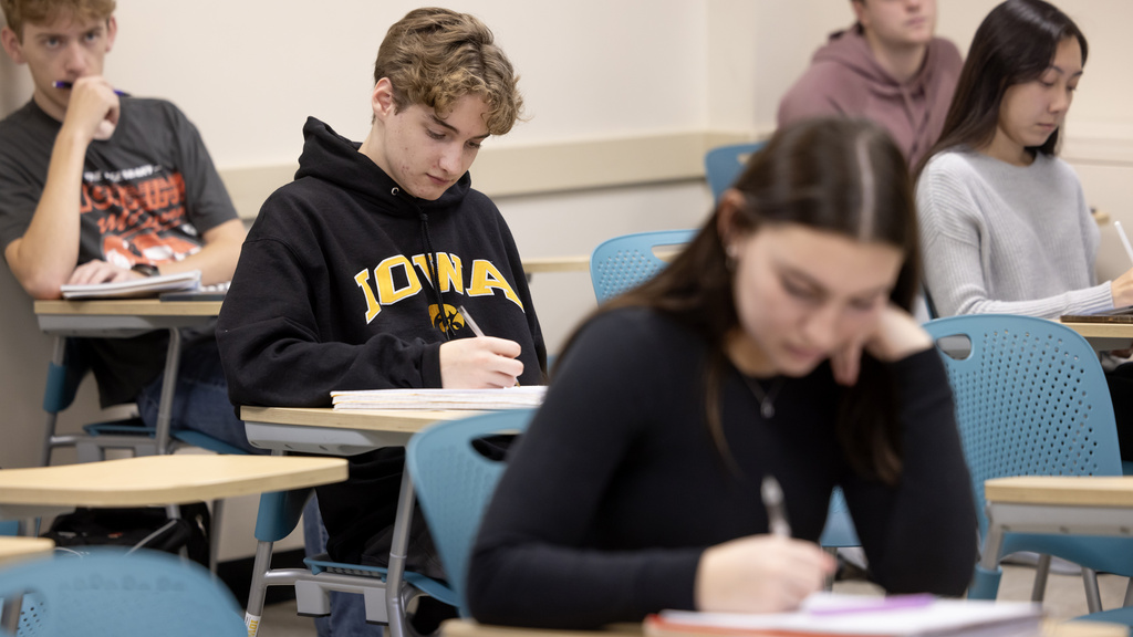 student wearing Iowa sweathshirt in class at desk writing